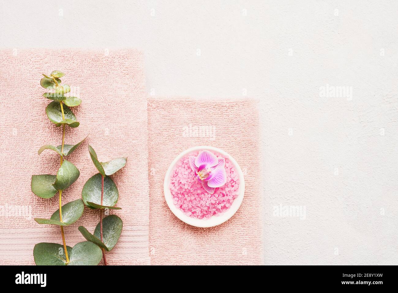 Serviettes roses roulées, sel de bain rose et branche d'eucalyptus sur fond de béton blanc. SPA, hygiène, bien-être bien-être, concept de soins du corps. Copier la flèche Banque D'Images