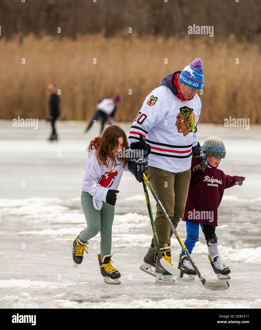 Père avec deux jeunes filles jouant au hockey sur glace sur un lac gelé Banque D'Images