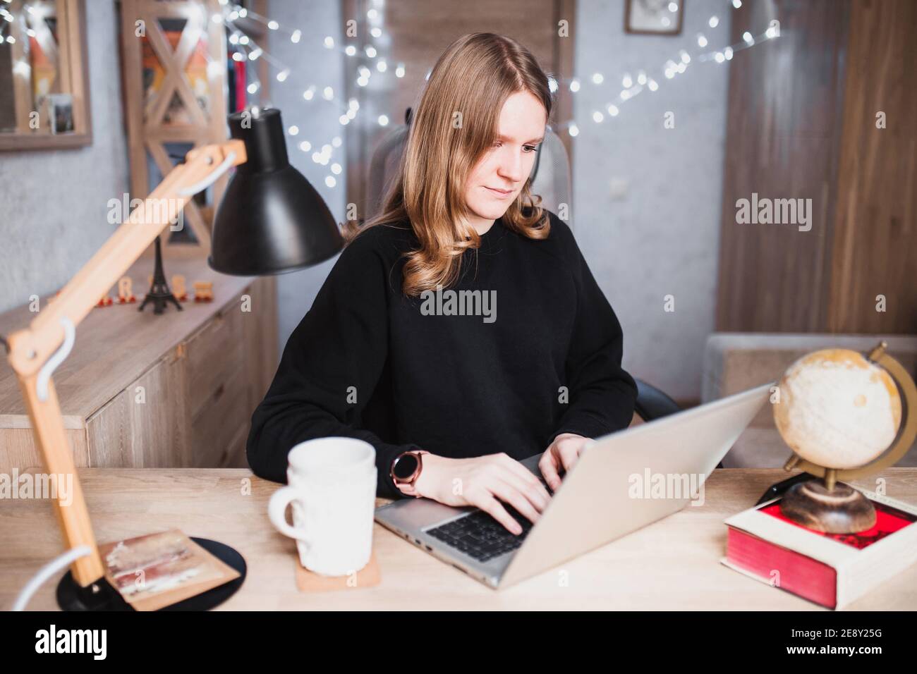 Jeune fille dans une chambre confortable à une table avec un ordinateur portable réserver un voyage Banque D'Images