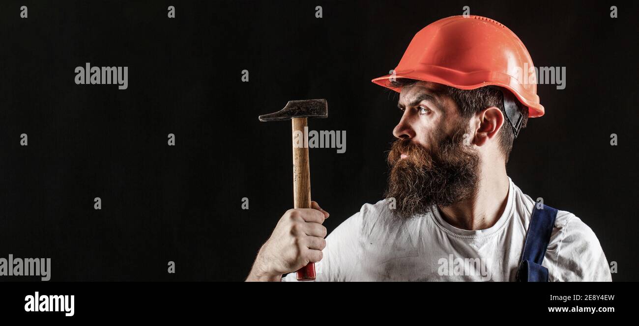 Services de handyman. Industrie, technologie, constructeur, concept. Homme barbu travailleur avec barbe, casque de construction, casque de sécurité. Marteler au marteau. Constructeur dans Banque D'Images