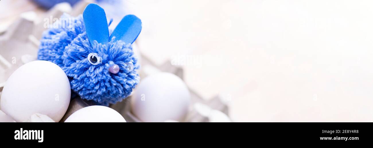 Ce lapin bleu est fait de pompons pour le décor de Pâques à la main. Lapin de Pâques et œufs blancs sur un stand projet d'art pour enfants. Concept DIY. Banque D'Images