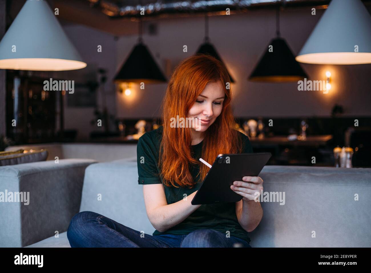 Jeune créatrice designer femme dans des lunettes tenant stylet dessin sur une tablette numérique dans un café moderne Banque D'Images