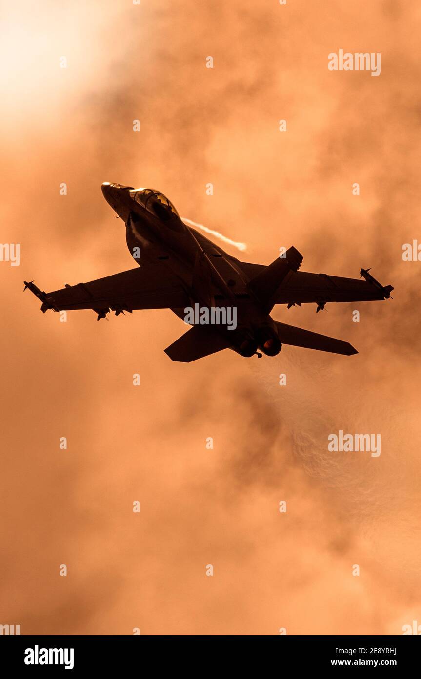 US Navy F/A18 Super Hornet grimpant dans un ciel de coucher de soleil, montrant l'air perturbé ou eflux dans son sillage. Banque D'Images
