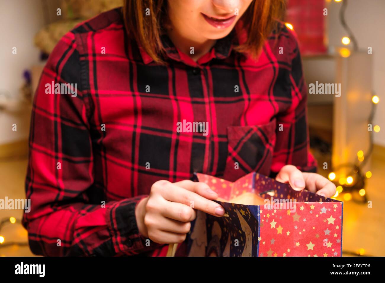 Une femme heureuse dans une chemise rouge ouvre un cadeau de vacances dans le paquet avec la lumière à l'intérieur. Concept anniversaire ou fête de la Saint-Valentin. Banque D'Images