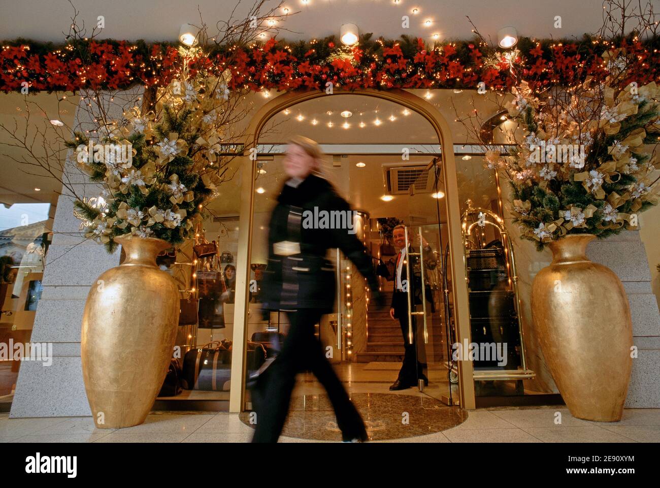 Femme méconnaissable quittant la boutique de luxe avec une décoration de noël dorée, le propriétaire de la boutique ouvre la porte au client. Banque D'Images