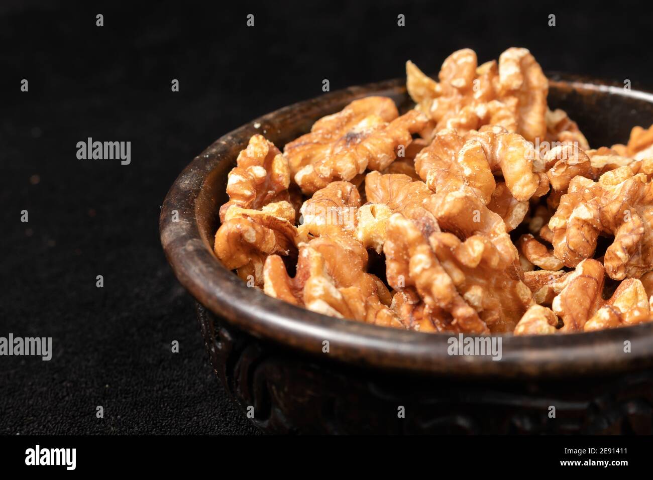 Bol en bois sculpté avec graines de noyer pelées sur fond noir. vue à 45 degrés. Banque D'Images