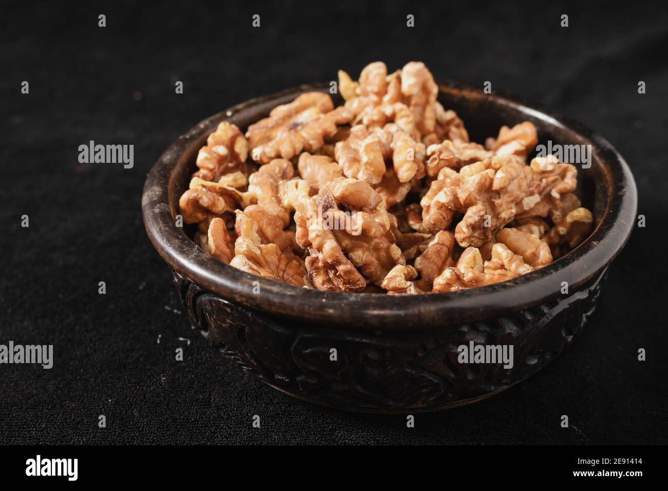 Bol en bois sculpté avec graines de noyer pelées sur fond noir. vue à 45 degrés. Banque D'Images