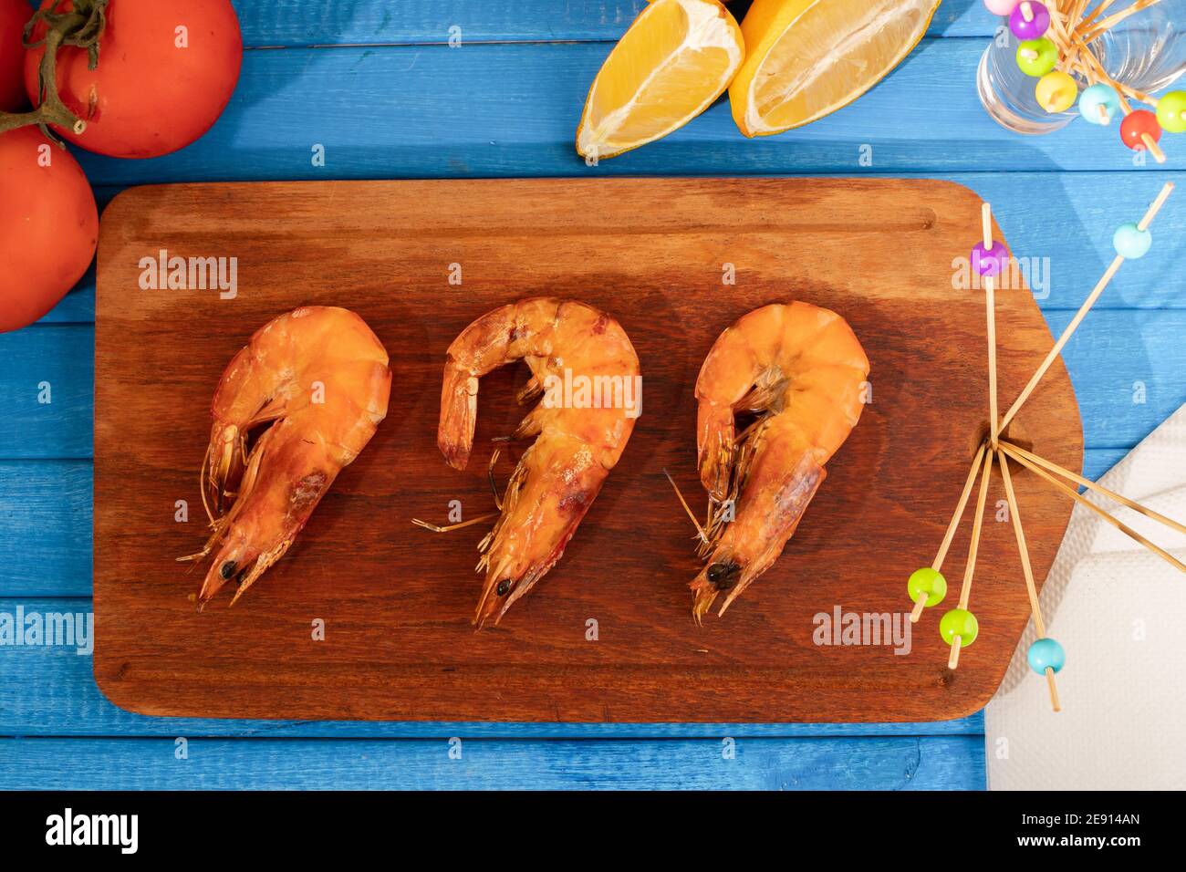 Crevettes rôties entières sur un plateau en bois, sur une table bleue. Nourriture d'été, fraîche et naturelle. Banque D'Images