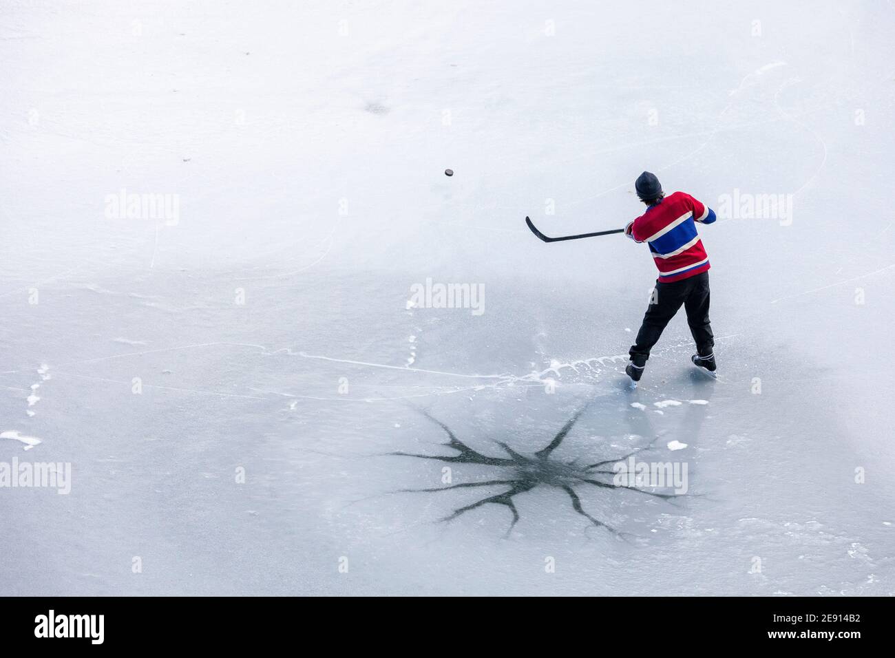 D'un homme anonyme en uniforme de tir de rondelle avec bâton en jouant au hockey près de crack dans la glace du lac gelé en Colombie-Britannique, Canada Banque D'Images