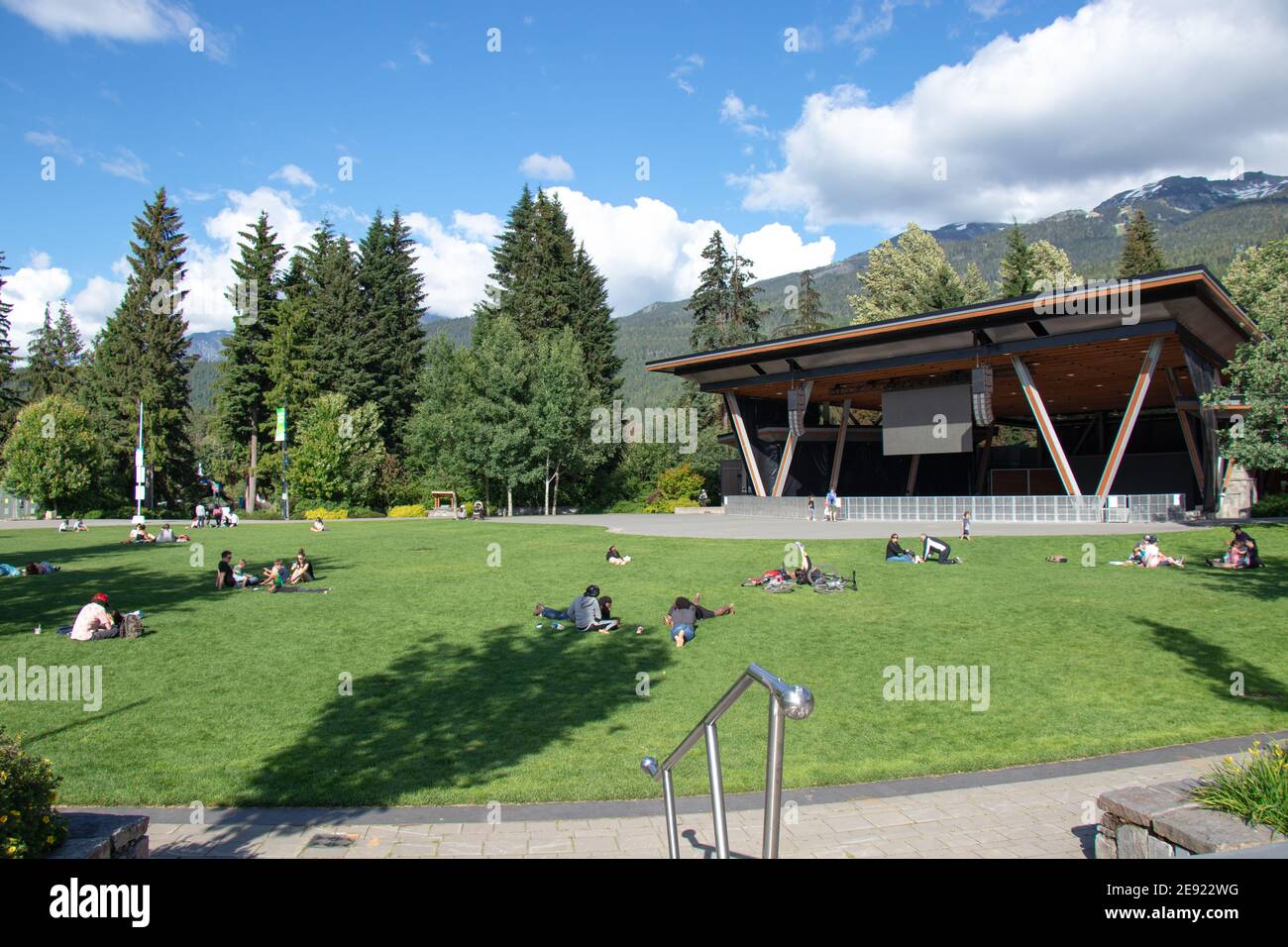 Whistler, Canada - le 5,2020 juillet : les gens sont assis sur la pelouse verte lors d'une journée ensoleillée dans le village de Whistler avec des montagnes en arrière-plan Banque D'Images