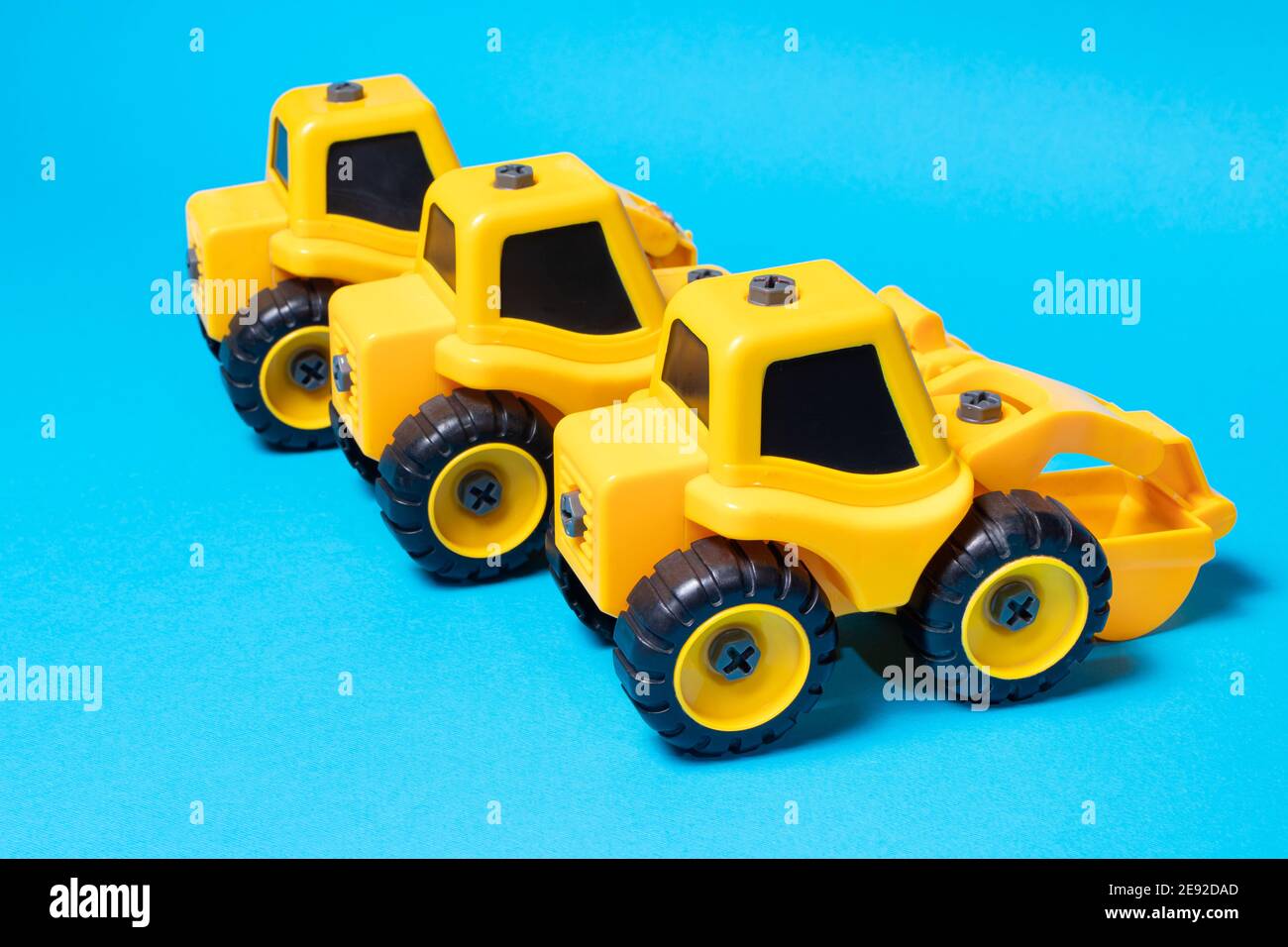 Trois tracteurs jaunes sur fond bleu, jouets de construction d'une voiture pour garçon pour un magasin de jouets. Banque D'Images