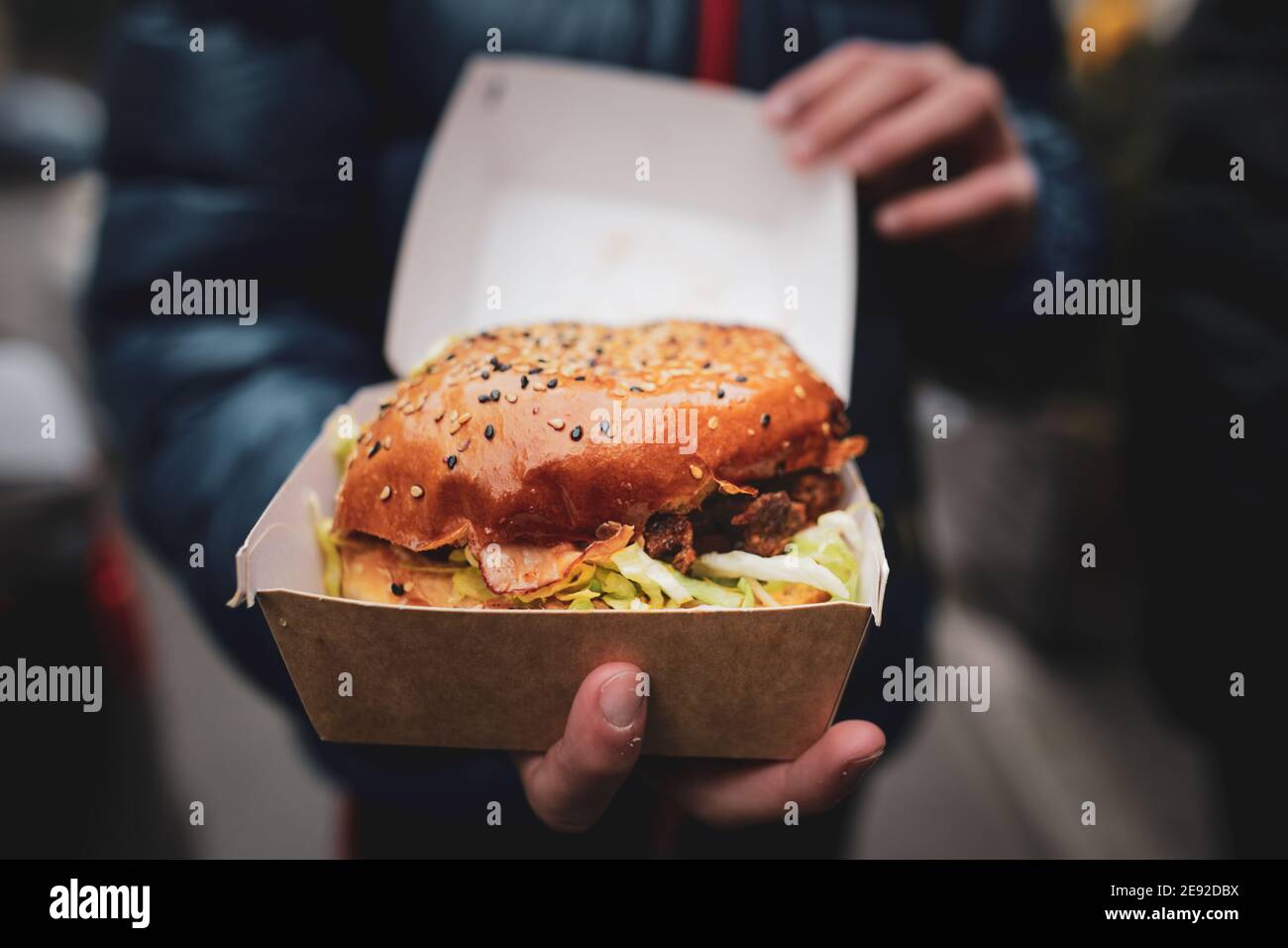 Faible profondeur de champ (mise au point sélective) avec les mains d'un jeune homme tenant un hamburger en boîte. Banque D'Images