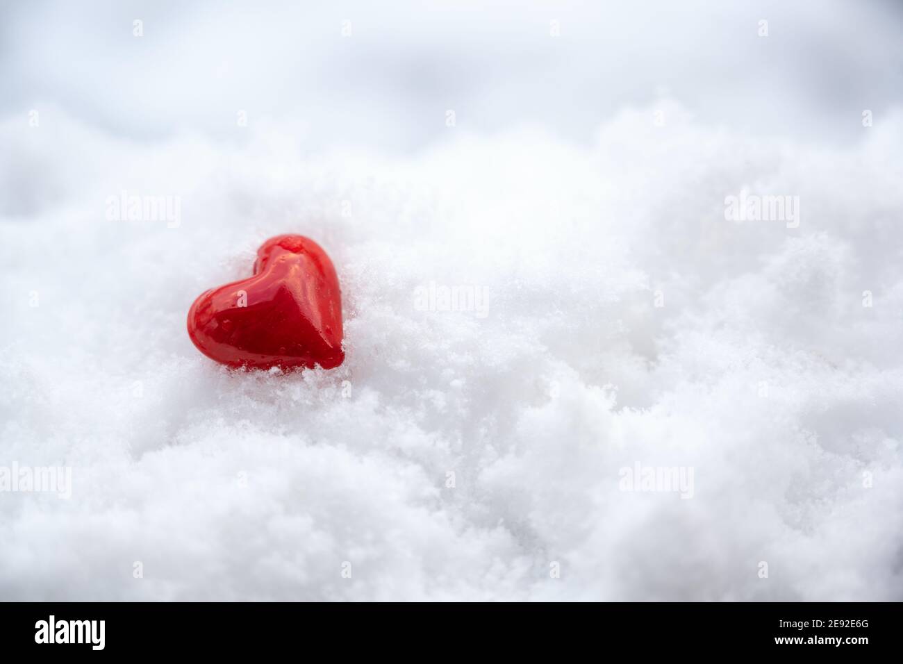 Petit coeur rouge de verre couché dans la neige blanche, symbole de l'amour pour la Saint Valentin avec grand espace de copie, mise au point sélectionnée, profondeur de champ étroite Banque D'Images