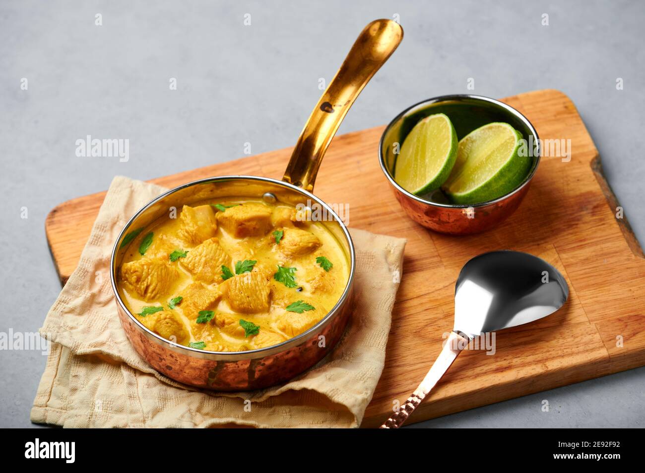 Poulet Korma dans un récipient en cuivre sur une table en béton gris. Cuisine indienne plat de cari à la viande avec masala au lait de coco. Cuisine asiatique Banque D'Images