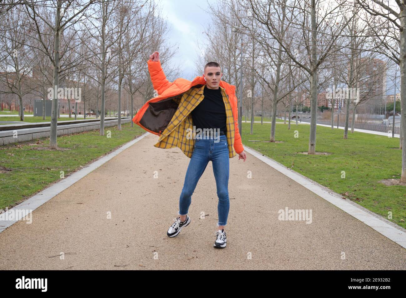 Beau jeune homme portant du maquillage et des écouteurs, dansant sur un sentier de parc. Type androgyne non binaire. Banque D'Images