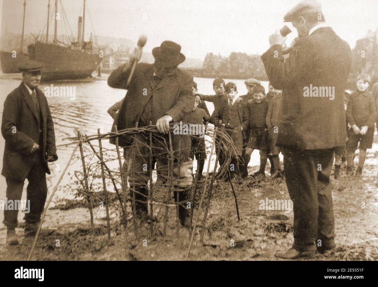 Whitby (Yorkshire UK,) cérémonie traditionnelle de haies Horngarth ou Penny 1906. Une photographie historique montrant la cérémonie annuelle de plantation de la haie de Penny ou Horngarth dans la rivière Esk à Whitby, dans le North Yorkshire, au Royaume-Uni, en 1911. À la fin de la haie, l'homme avec la corne souffle sur vous (sortez) en défiant la marée de détruire la haie de penny dans trois marées, en ligne avec une légende locale. La coutume a lieu au sein du sein d'Abraham la veille de l'Ascension (40e jour après le dimanche de Pâques) , dans la boue de la rive est de l'Esk . Banque D'Images