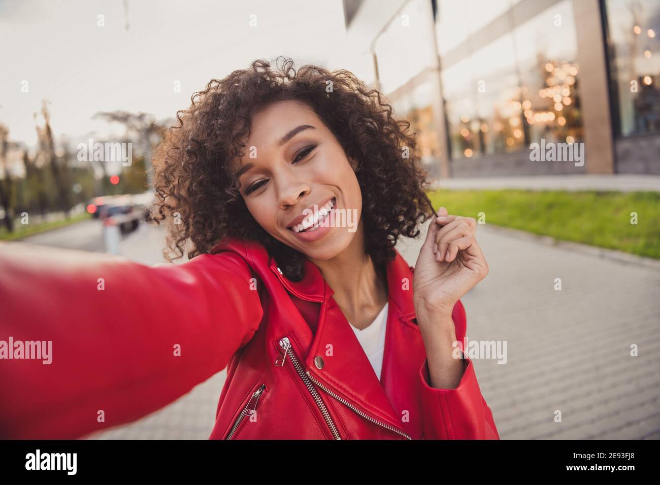 Photo de brillante jolie charmante femme ondulée porter une veste rouge enregistrement souriant bras de main de la vidéo se courber à l'extérieur de la rue de ville urbaine Banque D'Images