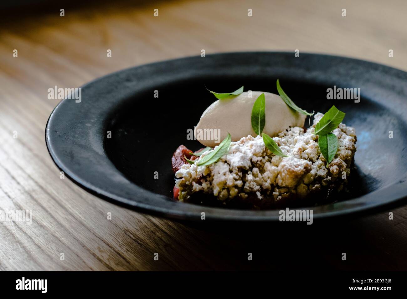 Assiette de sorbet et de tarte au rhubarbe recouverte de feuilles de menthe dans un plat noir sur une table en bois dans un restaurant Banque D'Images