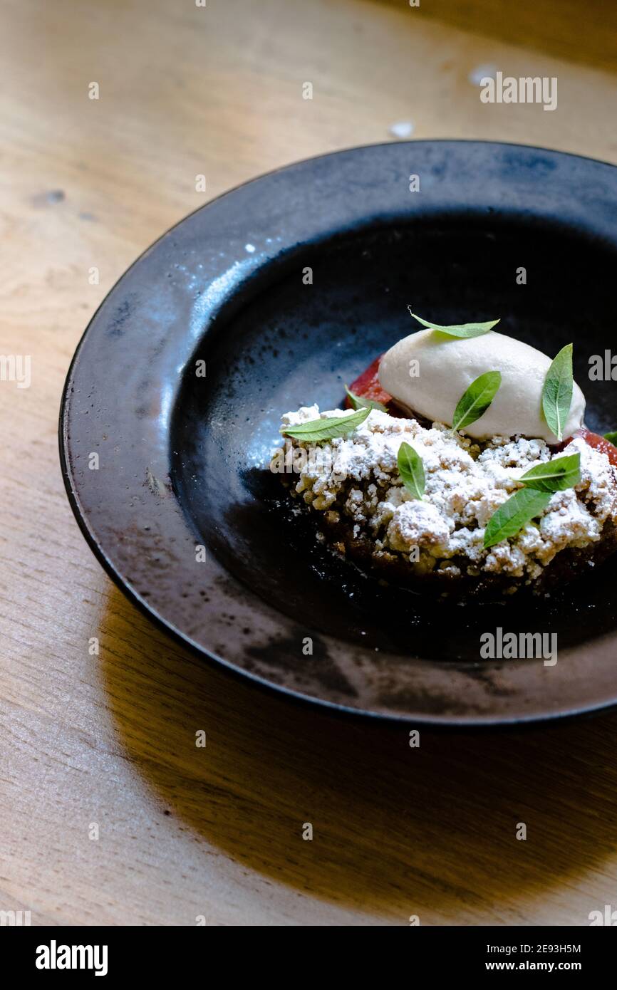 Assiette de sorbet et de tarte au rhubarbe recouverte de feuilles de menthe dans un plat noir sur une table en bois dans un restaurant Banque D'Images