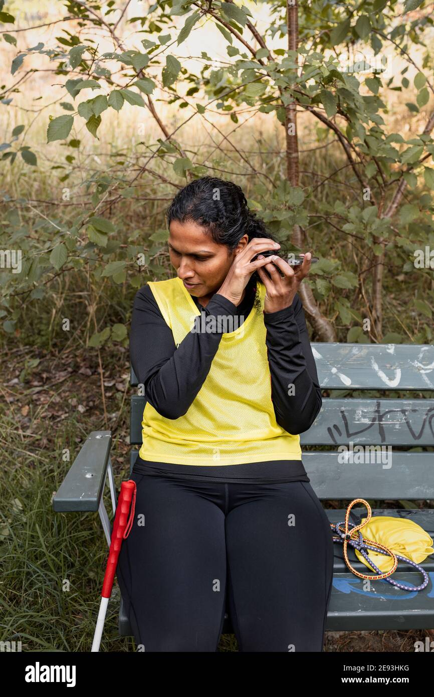 Femme malvoyante assise sur un banc et utilisant un téléphone cellulaire Banque D'Images