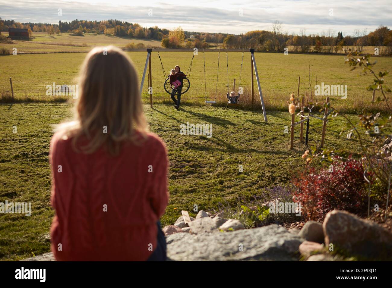 Femme regardant le reste de sa famille jouant dans le jardin Banque D'Images