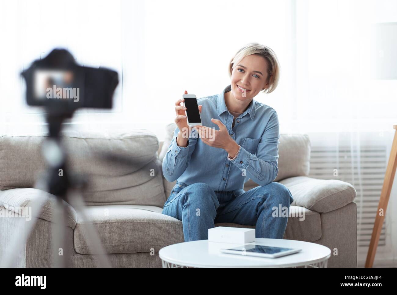 Vlogger femme millénaire qui passe en revue le nouveau modèle de smartphone à l'aide d'un appareil photo reflex numérique professionnel à la maison Banque D'Images