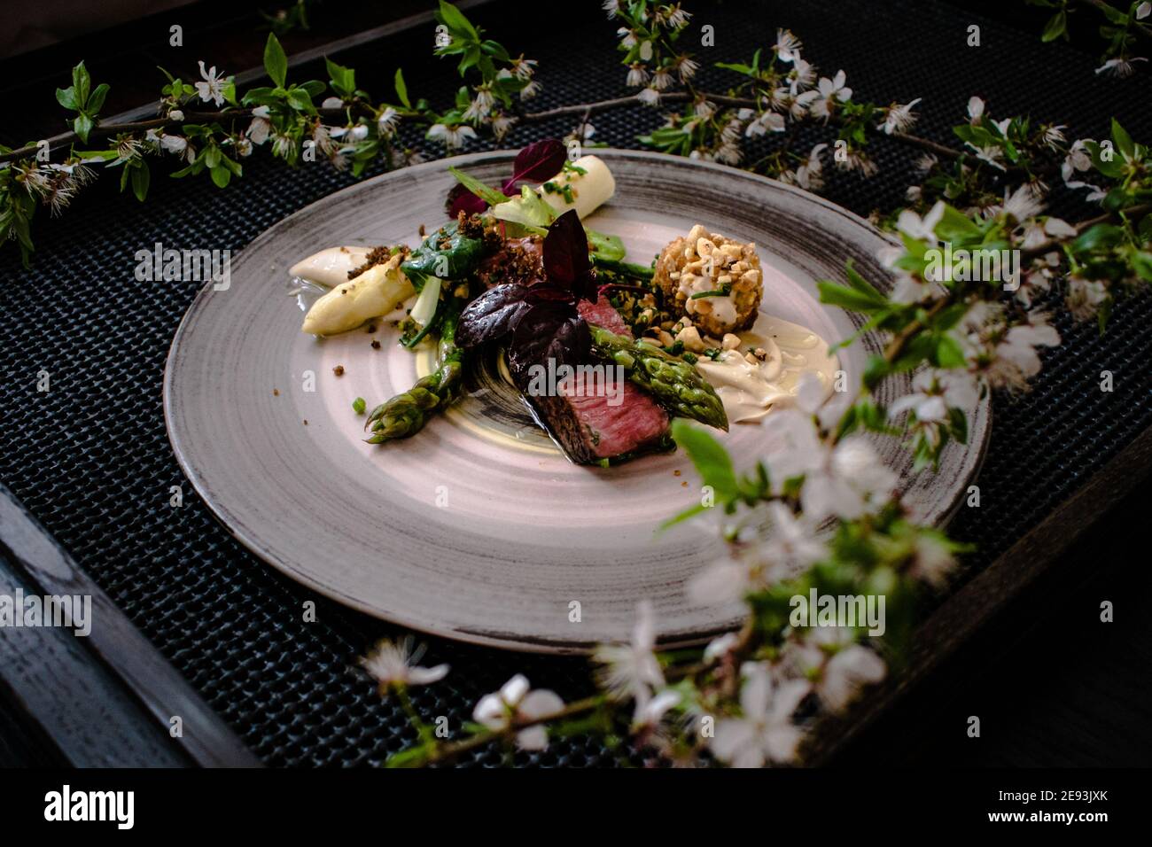 Plat de steak d'autruche avec asperges blanches et vertes, légumes verts et sauce sur une assiette sur une table en bois dans un restaurant Banque D'Images