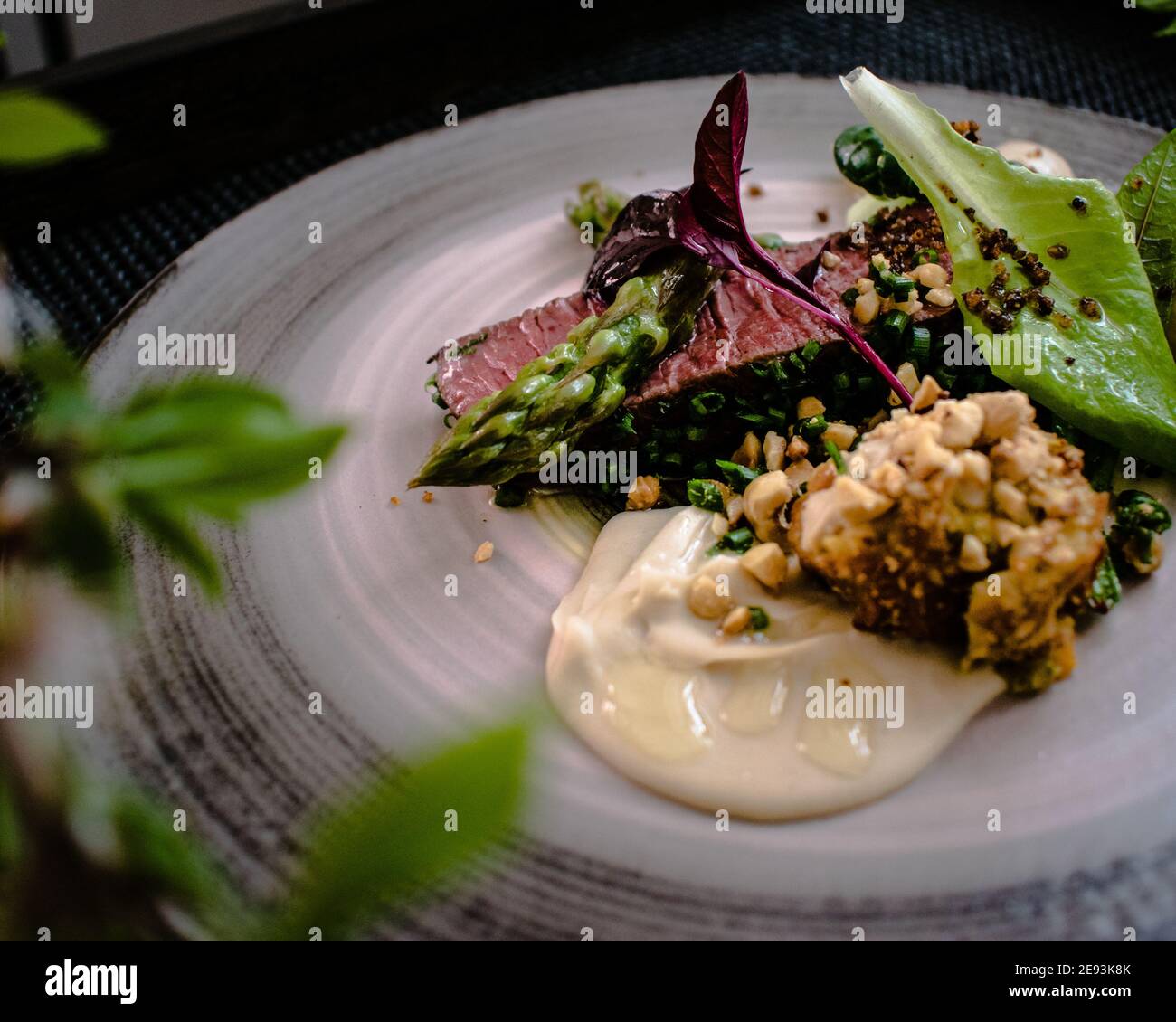 Plat de steak d'autruche avec asperges blanches et vertes, légumes verts et sauce sur une assiette sur une table en bois dans un restaurant Banque D'Images