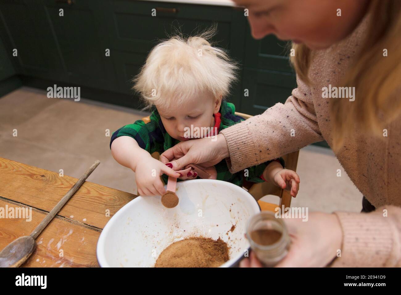 Jeune garçon aidant sa mère à ajouter des ingrédients dans un bol à mélanger dans la cuisine. Banque D'Images
