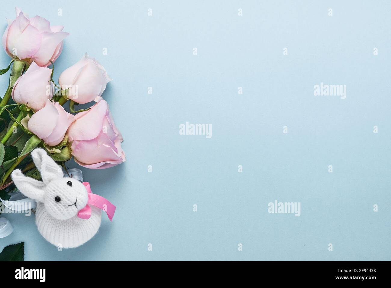 Bouquet de fleurs roses roses avec ruban et joli lapin de Pâques sur fond bleu. Modèle de carte de vœux avec espace de copie Banque D'Images