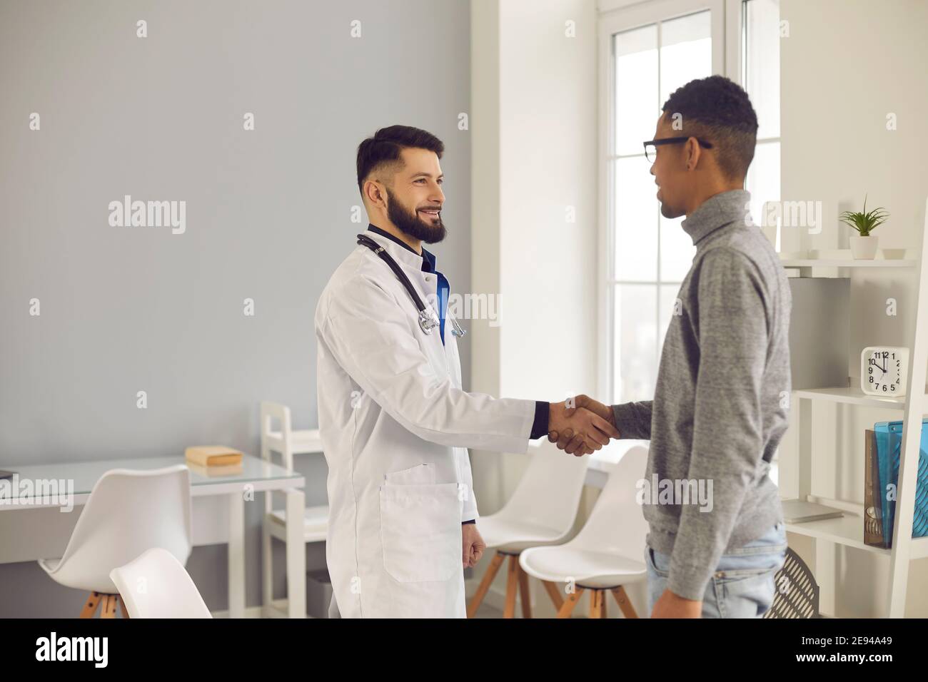 Jeune médecin souriant accueillant un nouveau patient dans son bureau à la clinique ou l'hôpital Banque D'Images