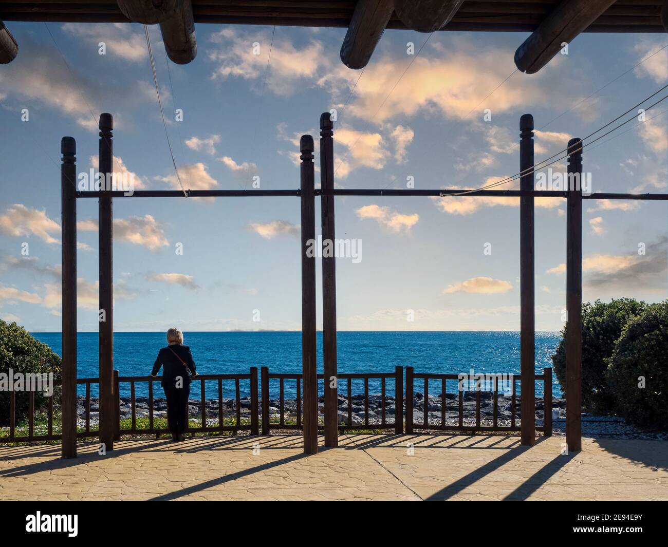 Une femme qui donne sur la mer sous un belvédère avec une pergola en bois par une journée d'hiver nuageux. Banque D'Images