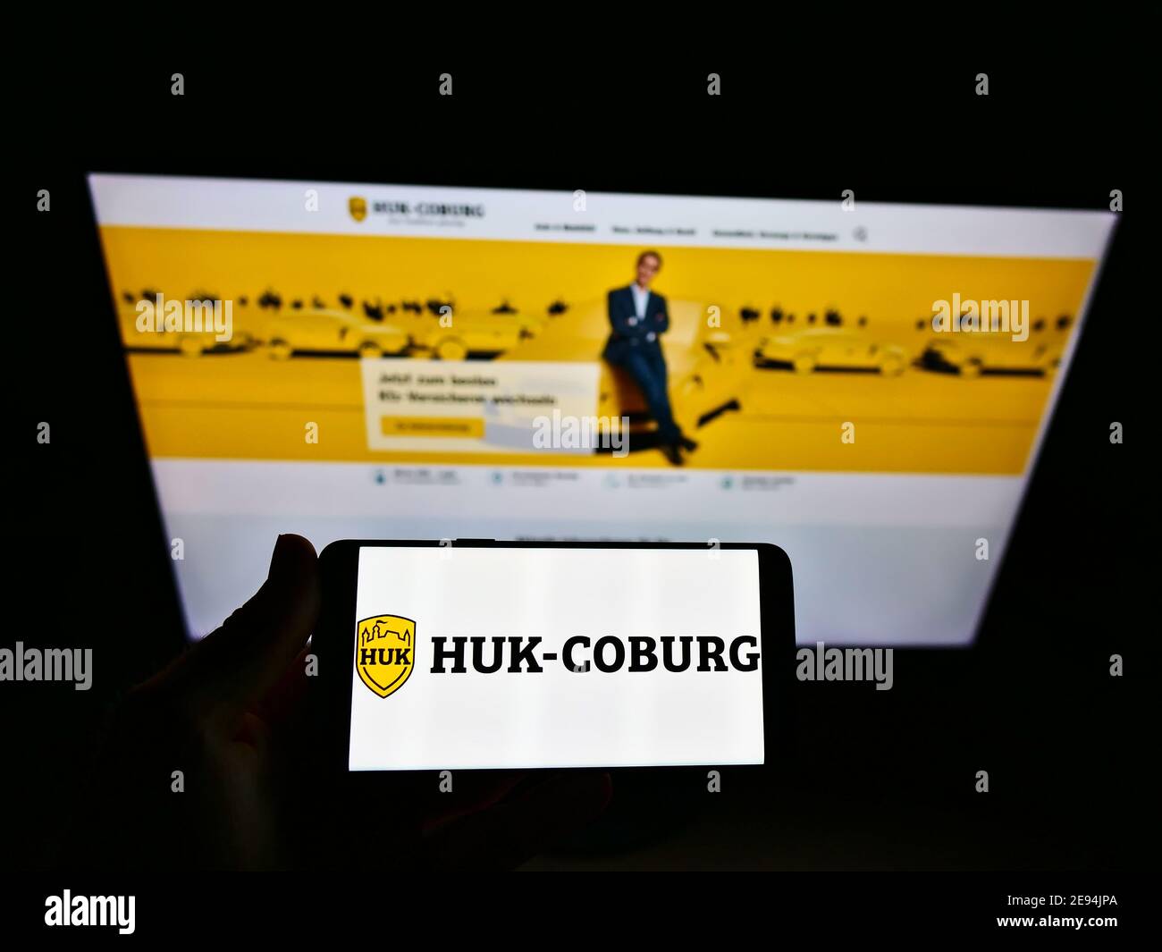 Personne portant un smartphone avec le logo de la compagnie d'assurance allemande HUK-Coburg exposé devant le site Web d'affaires. Mise au point sur l'écran du téléphone. Banque D'Images