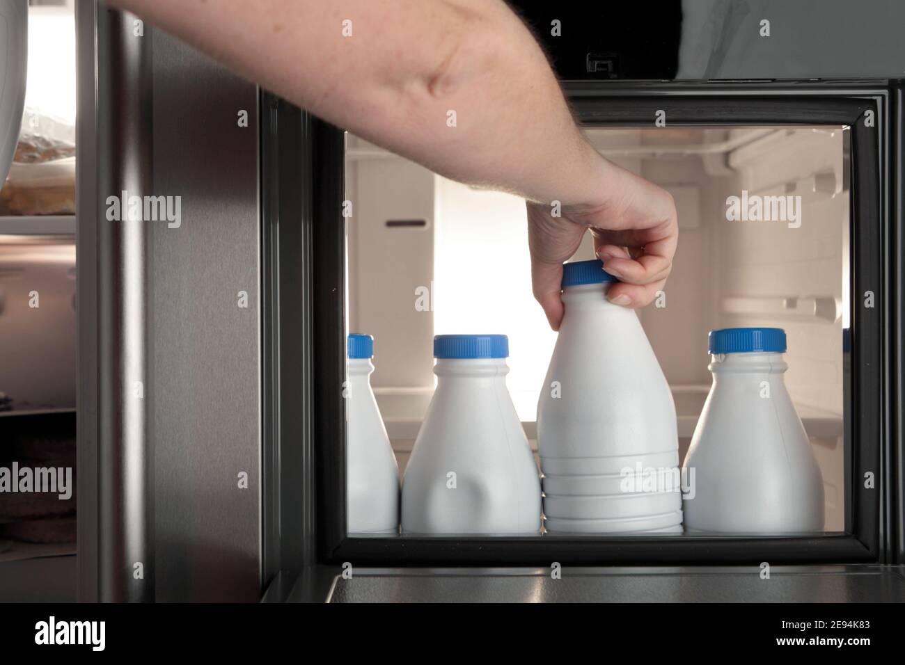 Main humaine prenant une bouteille de lait d'un réfrigérateur en passant par la petite porte Banque D'Images