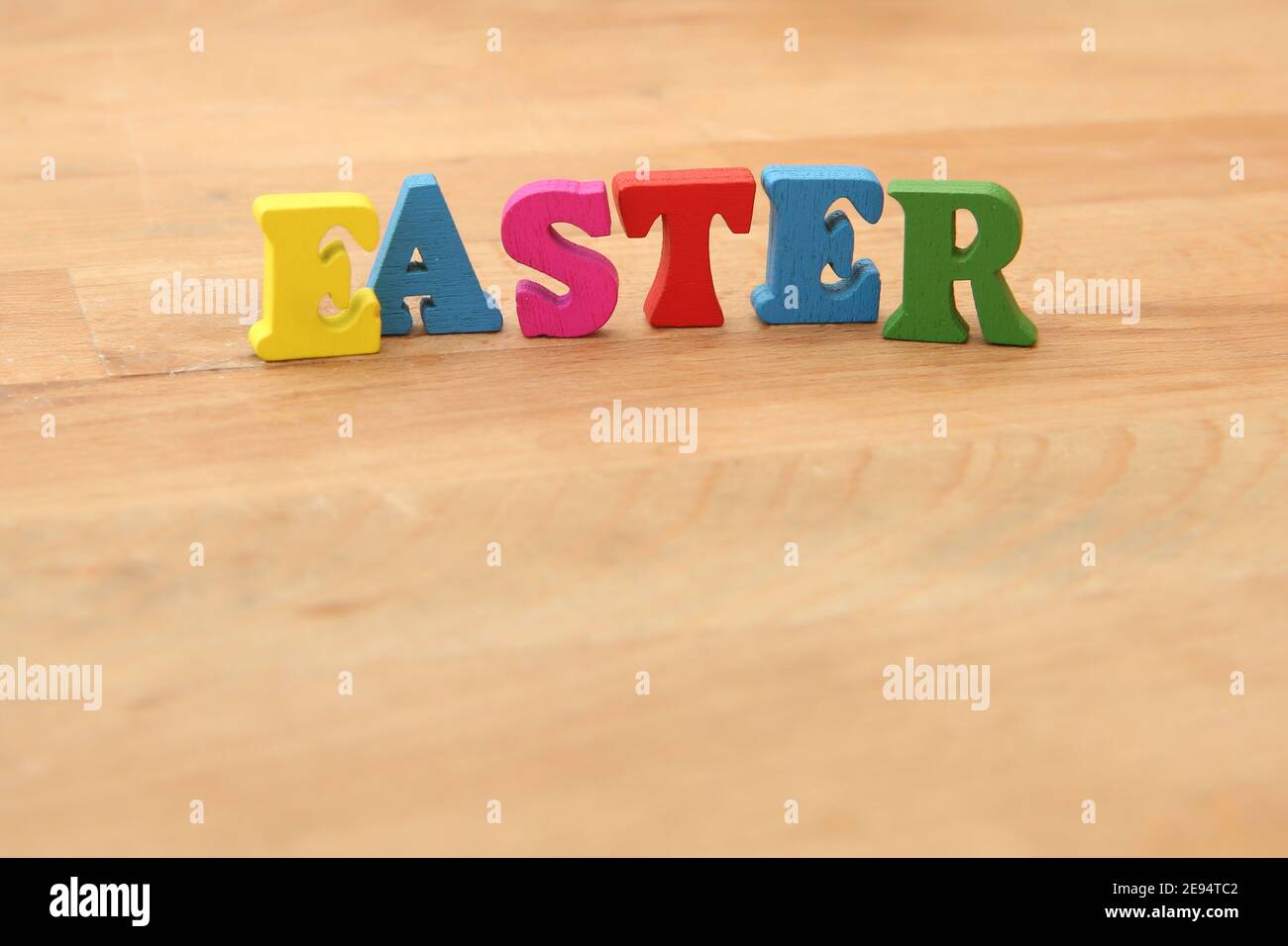 Easter orthographié en lettres de bois colorées sur fond beige en bois naturel. Banque D'Images