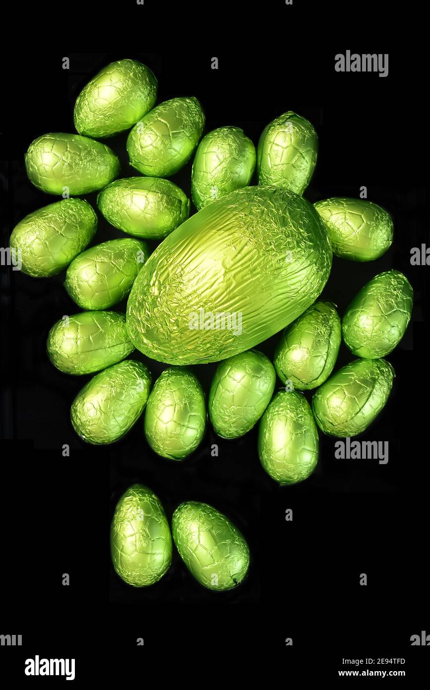 Pile ou groupe de plusieurs couleurs et de différentes tailles d'oeufs de pâques au chocolat enveloppés de papier d'aluminium coloré dans le pastel et le vert lime avec un gros oeuf vert. Banque D'Images