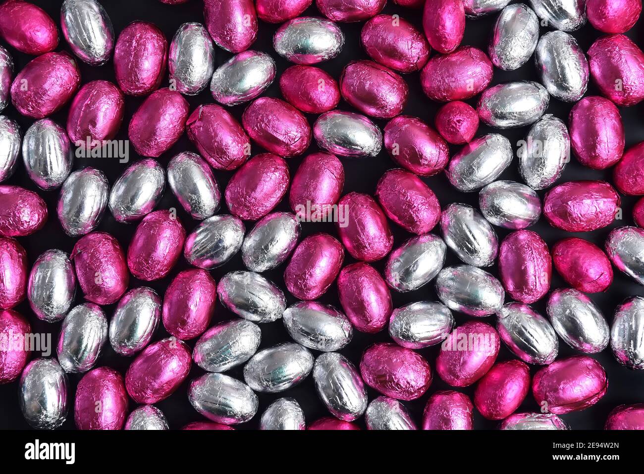 Œufs de pâques au chocolat, enveloppés de papier d'aluminium rose et argent, sur fond noir. Banque D'Images