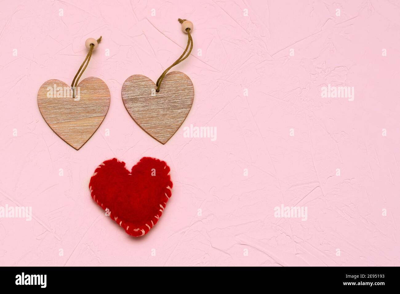 Deux coeurs en bois et une laine artisanale rouge sur fond texturé rose. Concept pour la Saint-Valentin, l'amour, le mariage. Banque D'Images