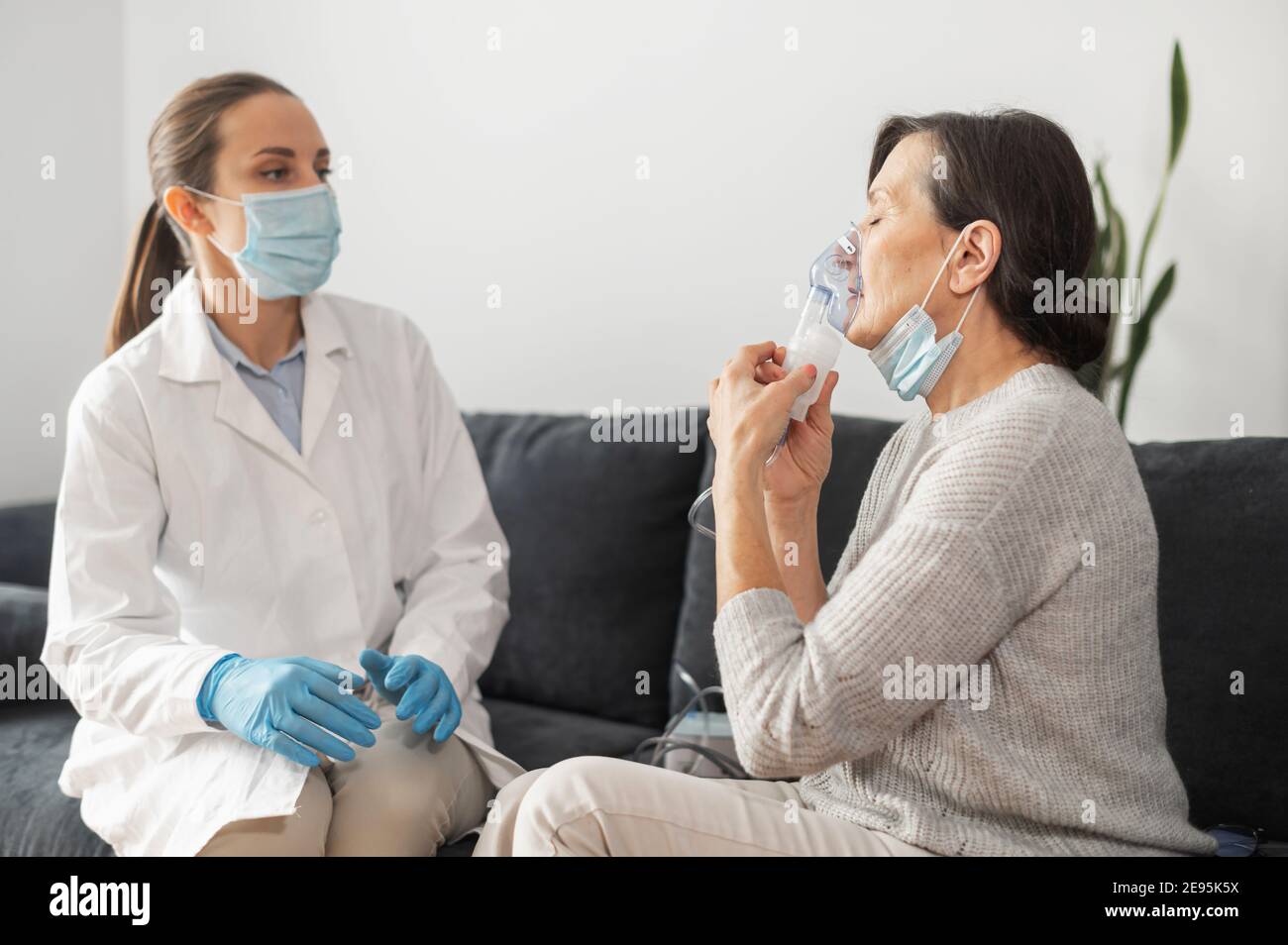 Une femme médecin, infirmière portant une blouse médicale et un masque  facial, met un masque à oxygène sur un patient sénior malade à la maison  pendant une pandémie. Soins de santé et