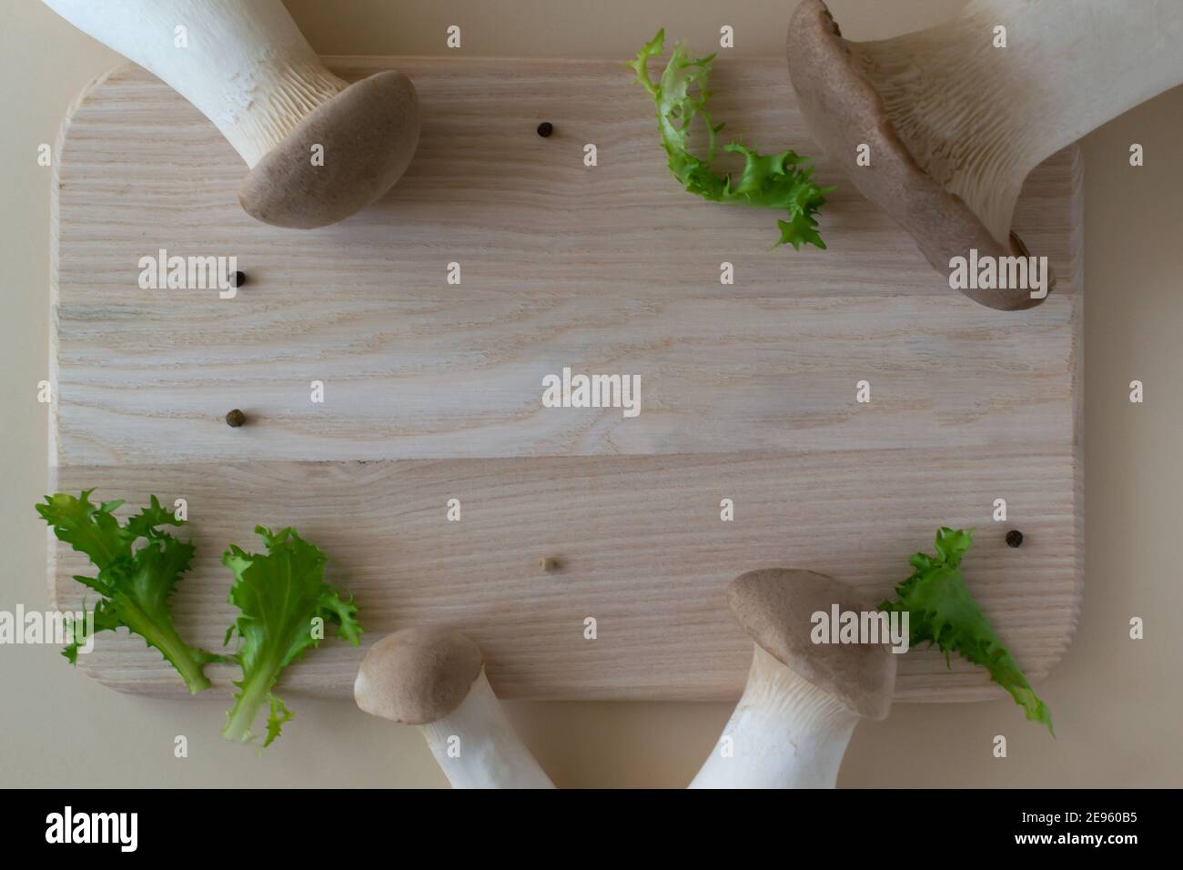 Champignons Eringi avec feuilles de laitue sur une planche à découper en bois sur fond pastel. Pleurotus eringi. Concept d'alimentation saine. Orientation horizontale. Banque D'Images