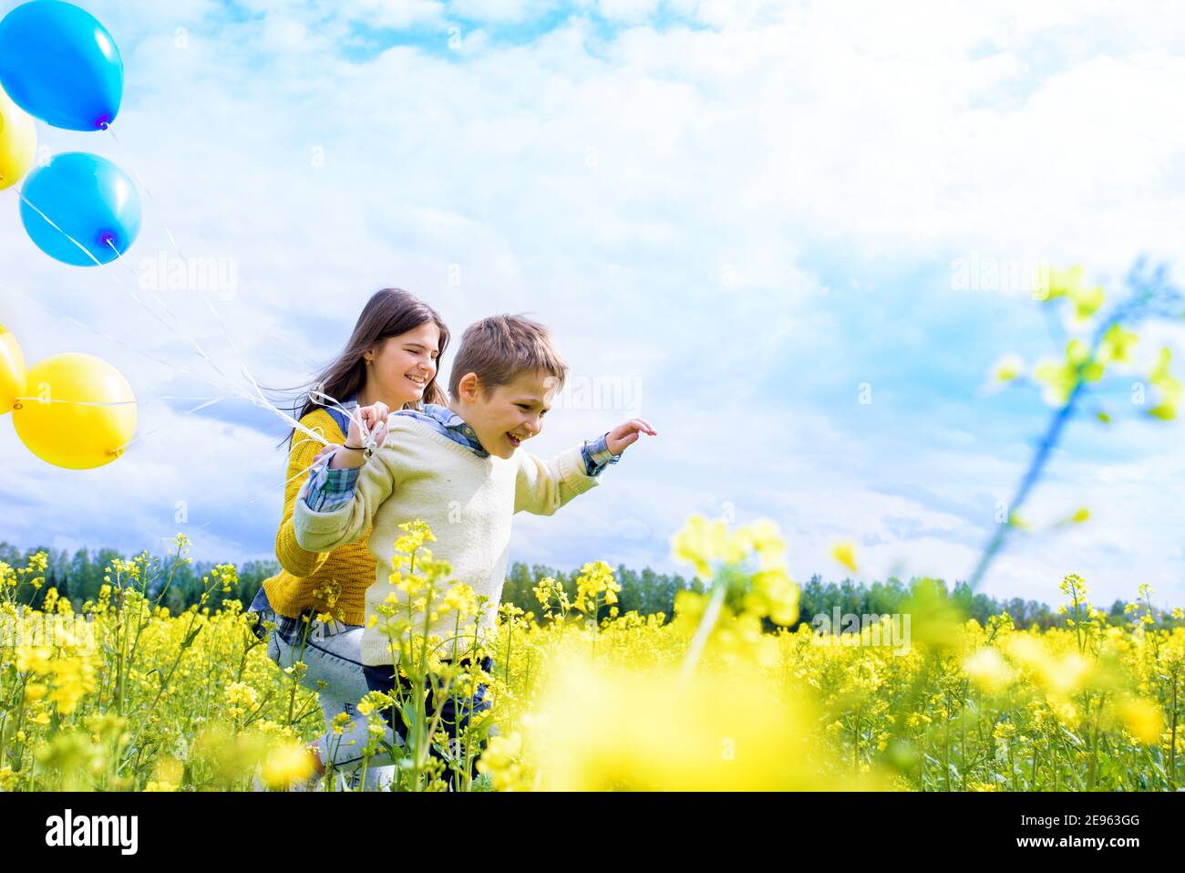 Jeune fille et garçon de 7 ans avec des ballons à l'extérieur.courir le long du champ jaune. Fleur de colza, concept de liberté.magnifique anniversaire d'été Banque D'Images