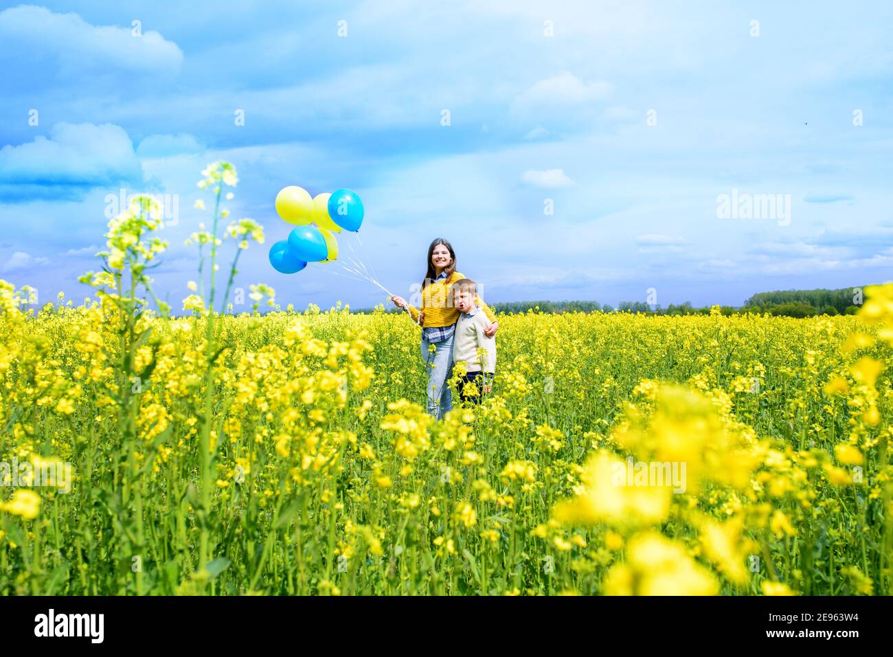 champ jaune, ciel bleu, nuages blancs. Courir de jolis enfants avec des ballons bleus et jaunes. Le concept de liberté, de vacances. Carte postale d'été. Banque D'Images