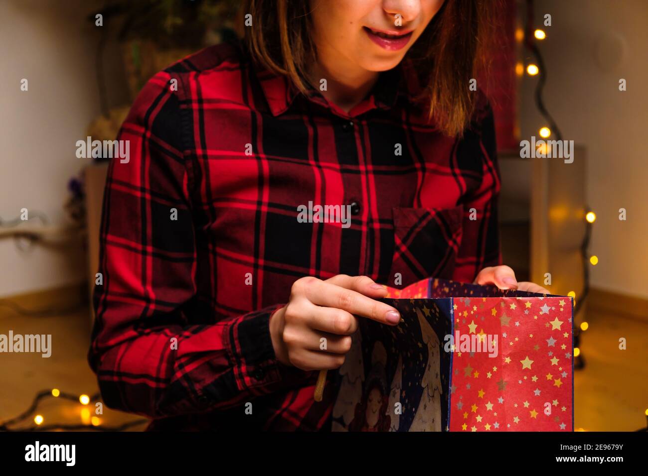 Une femme heureuse dans une chemise rouge ouvre un cadeau de vacances dans le paquet avec la lumière à l'intérieur. Concept anniversaire ou fête de la Saint-Valentin. Banque D'Images