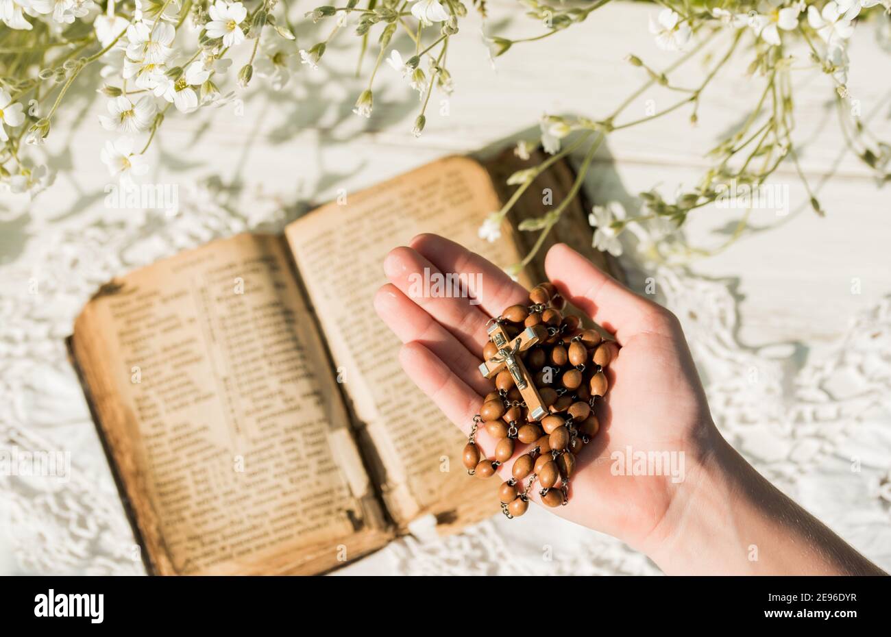 Les mains pliées dans la prière sur l'ancienne Sainte Bible. Arrière-plan en bois.mains et rosaire, prière, vieux livre aux pages jaunes. Fleurs blanches sur fond. Dans Banque D'Images