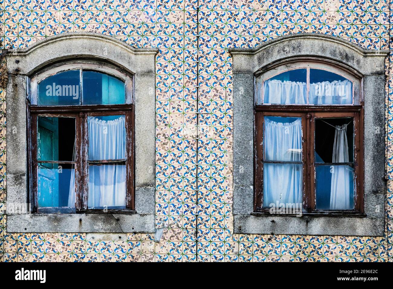 Gros plan de la façade traditionnelle portugaise de maison décorée par de beaux carreaux azulejo en céramique, deux vieilles fenêtres avec des rideaux bleus Banque D'Images