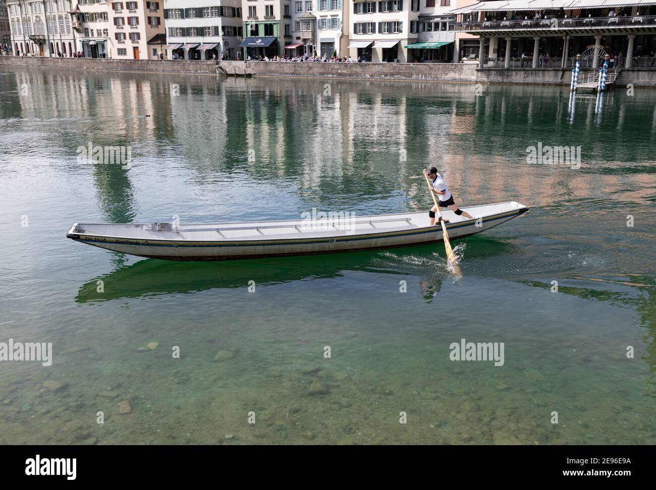 zurich, suisse - 25 avril 2019 : un jeune homme dans un t-shirt blanc pagaies debout dans un long barque le long du limmat, la rivière bleu-vert est v Banque D'Images