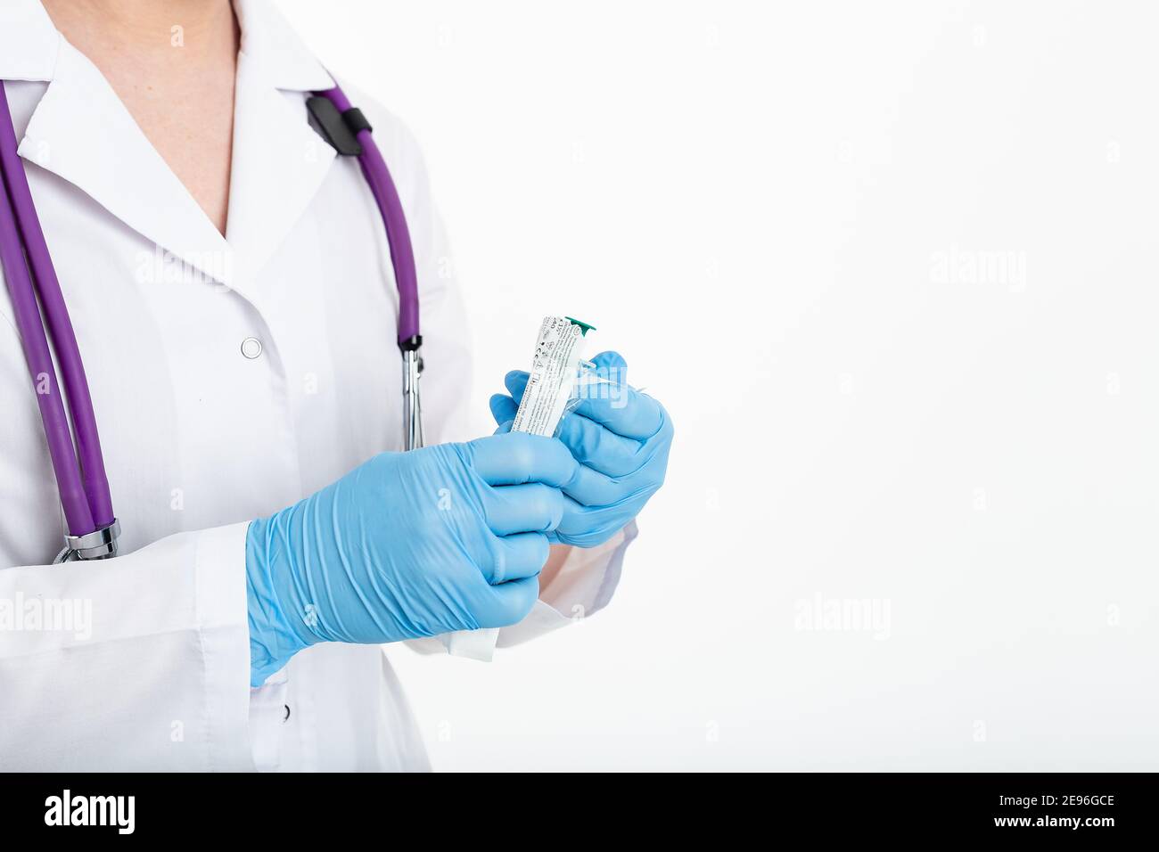 Une jeune infirmière dans un masque ouvre une seringue sur un fond blanc dans un manteau blanc, pour faire une vaccination, une injection. Le concept de vaccination et Banque D'Images