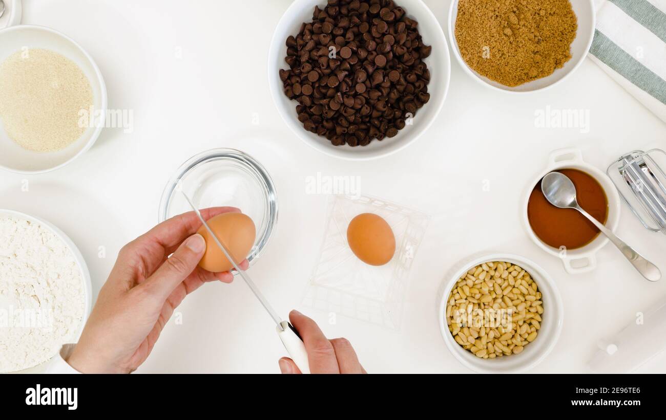 Recette de biscuits aux pépites de chocolat. Le chef coupe les œufs dans un bol. Gros plan sur une table de cuisine blanche pour préparer les ingrédients nécessaires à la cuisson Banque D'Images