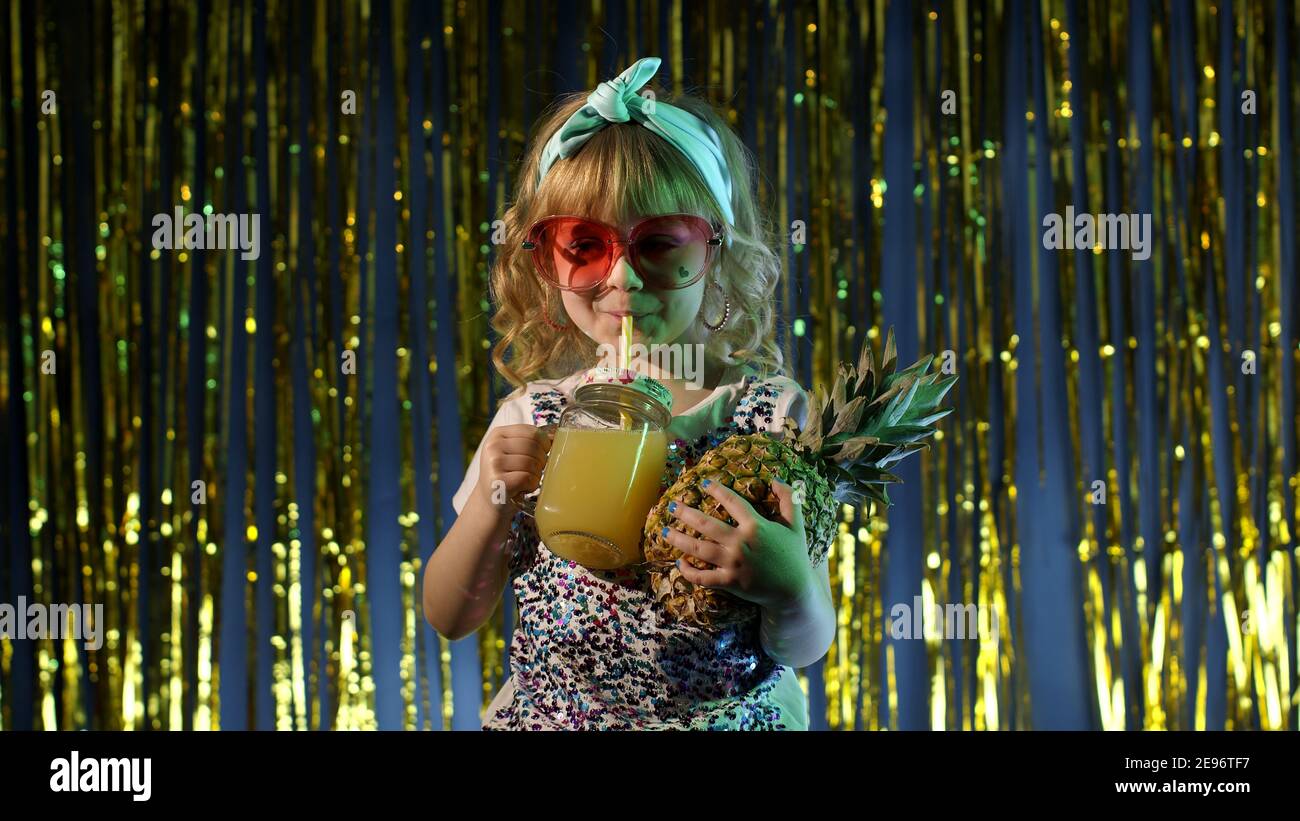 Portrait de mode, magnifique fille d'enfants dans la boîte de nuit  futuriste avec des lumières multicolores au néon. Enfant tendance et  élégant avec jus d'ananas. Style disco look sensuel clubber seul Photo