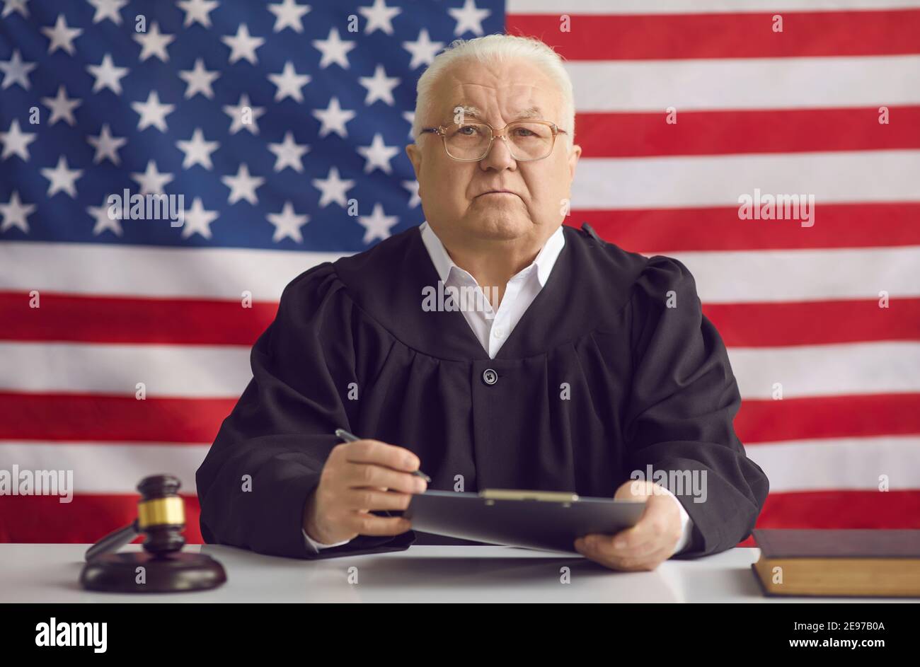 Un juge masculin sérieux et sage assis à table contre American arrière-plan drapeau Banque D'Images